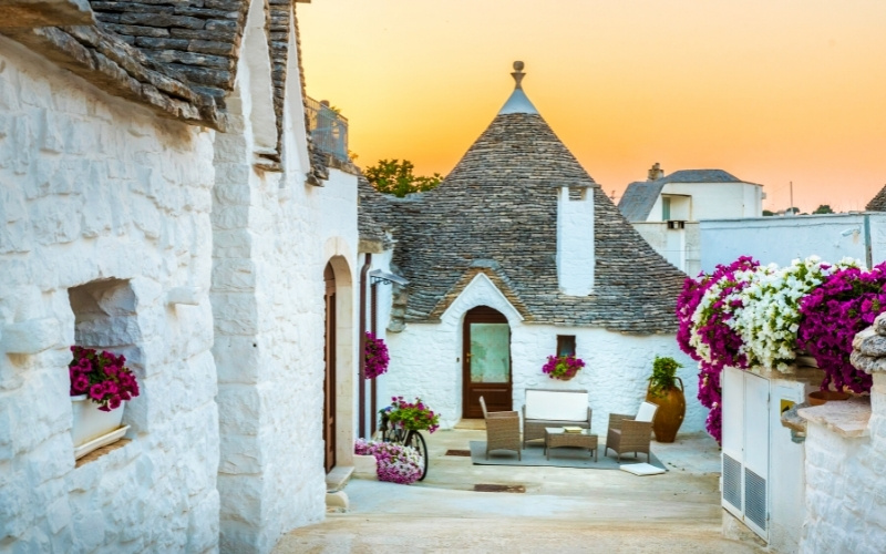 streetview of alberobello with the typical trulli houses and a sunset in the background. Alberobello is a good destination to travel locally in the off-season.
